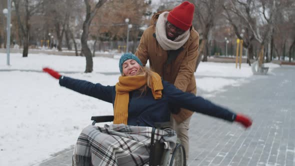 Happy Woman Riding Wheelchair with Help of Black Man