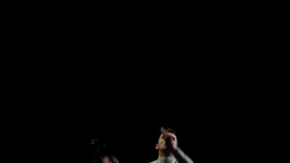 Male Gymnast on a Black Background in White Clothes Soars Into the Frame From Below and Makes