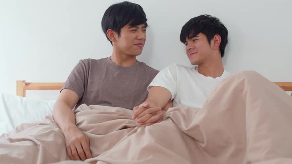 Handsome Asian gay couple talking on bed at home.