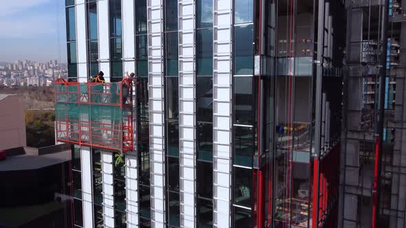 Workers On The Suspended Cradle Are Assembling The Skyscraper Exterior Elements