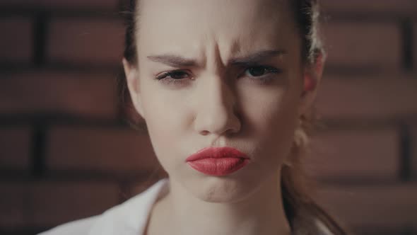 Beautiful Woman Frowning Face and Looking Into Camera on Brick Wall Background