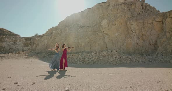 Female Musicians in Blowing Dresses Play the Violins on Nature at Cliff