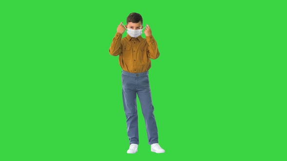 Little Boy Taking His Face Mask Off and Smiling at Camera on a Green Screen, Chroma Key.