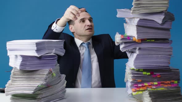 A Middle-aged Office Clerk Shifts Stacks of Papers on His Desk. Isolated Blue Background