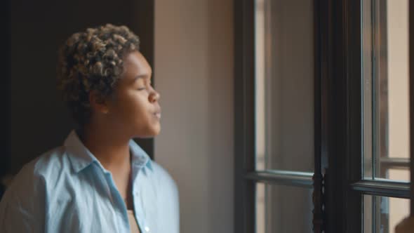 Young African Woman Standing By Window at Home Looking Happy and Content