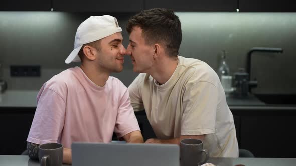 Loving Romantic Gay Couple Rubbing Noses Watching Movie Online on Laptop in Kitchen