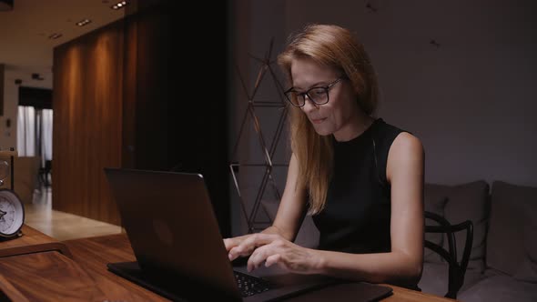 A Woman in a Home Office Sitting at a Table Types Text on a Laptop