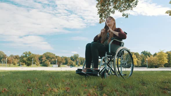 Young Caucasian Disabled Woman Listening Music and Hand Dancing Under the Tree. Wide Angle