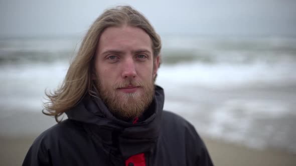 Closeup Portrait of Bearded Caucasian Man Standing Against of Stormy Ocean Thinking of Surfing on