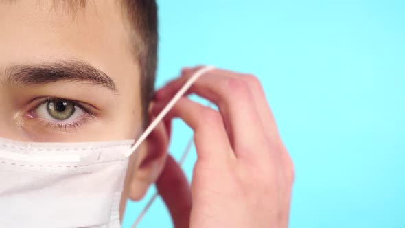 Sad young patient wears a medical mask on a bright blue background to protect breathing. 