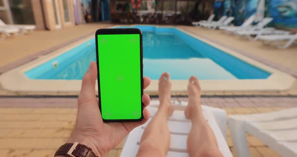 POV Male Hand Holding Smartphone with Green Screen Relaxing Near Pool