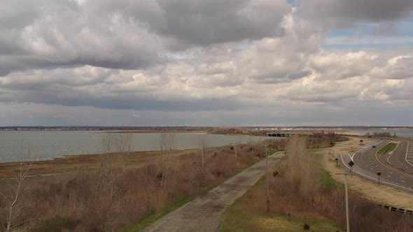 An aerial drone view on a cloudy day, over a dirt road which is near a bay. The drone camera bloom u