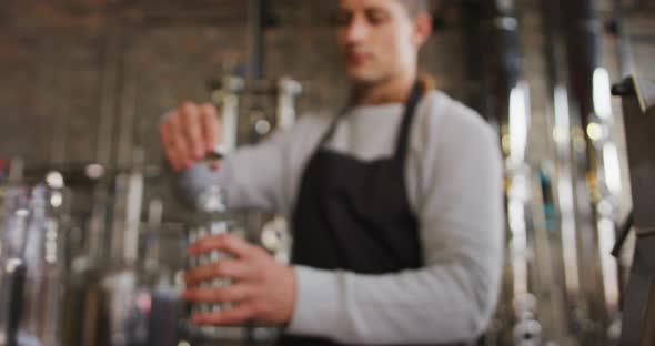 Caucasian man working at gin distillery, wearing apron, fastening lid on bottle of gin