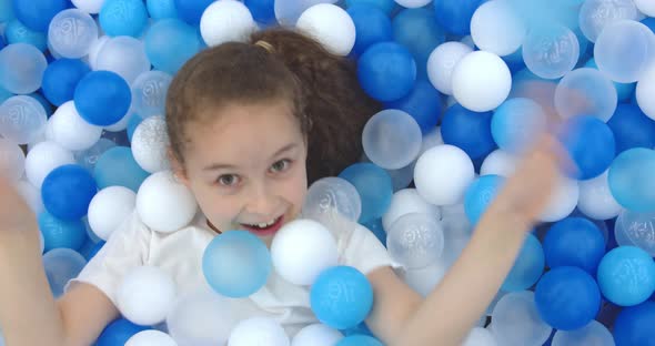 Portrait of a Cheerful Little Girl Smiling Child Jumps Out of Children's Plastic Ballskid Looks at
