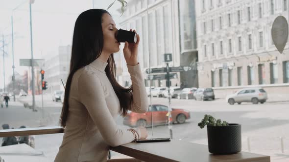 Young Woman Using Smartphone Sitting in Cafe Near the Big Window and Watching City Life