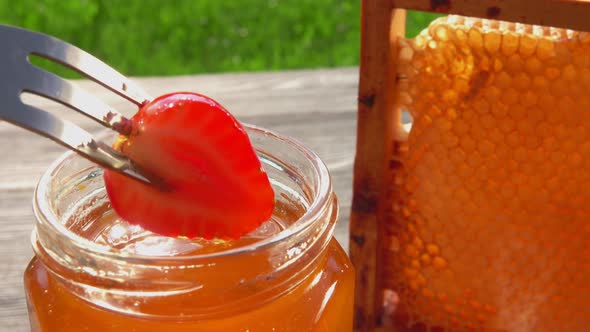 Fork with a Delicious Strawberry is Dipped Into Honey on the Jar