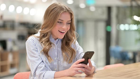 Excited Businesswoman Celebrating Success on Smartphone in Office 