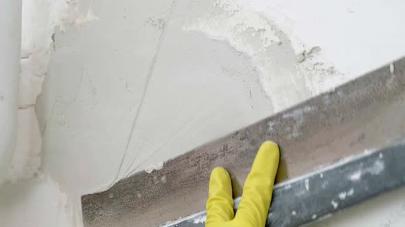 Plasterer Man Holding Putty Knife is Spackling Patching a Hole in White Wall