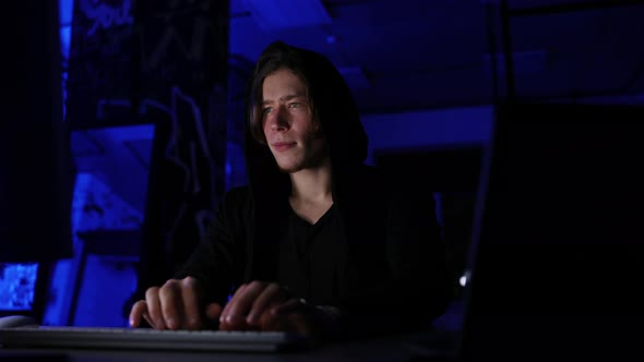 Medium Shot Portrait of Hidden Hacker Man Wearing Sweatshirt with Hood Engaged in Hacking Into