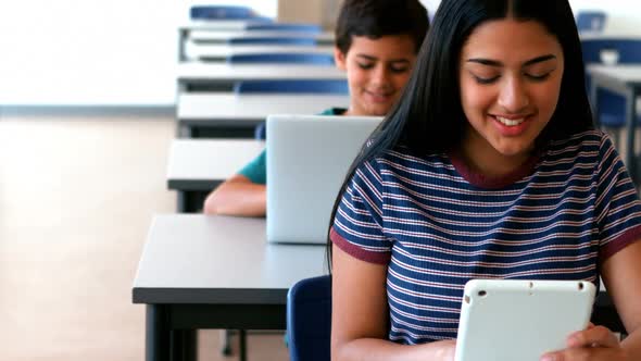 Schoolgirl and schoolboy using laptop and digital tablet while studying in classroom