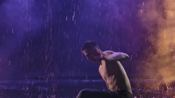 A Man Practicing Capoeira in a Dark Room Among Raindrops and Splashing Water. Smoky Background with