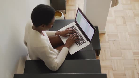 Happy african american woman sitting on stairs, using laptop