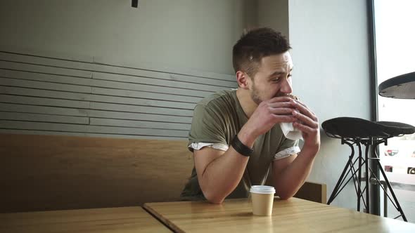Young Handsome Caucasian Male in Olive Tshirt Sitting at Cafe Eating Sandwich in Slowmotion