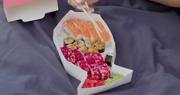 at a Picnic in the Woods a Girl is Eating Sushi with Chopsticks on a Blue Blanket