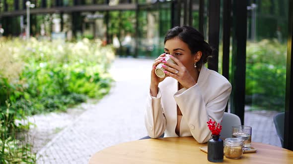 Young Business Woman Holding and Drinking Coffee in Street Cafe in City