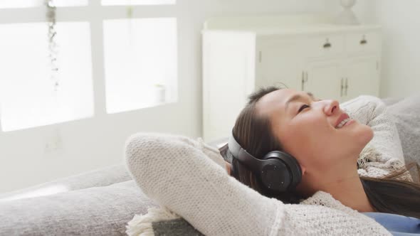 Happy asian woman lying on sofa, resting with headphones at home