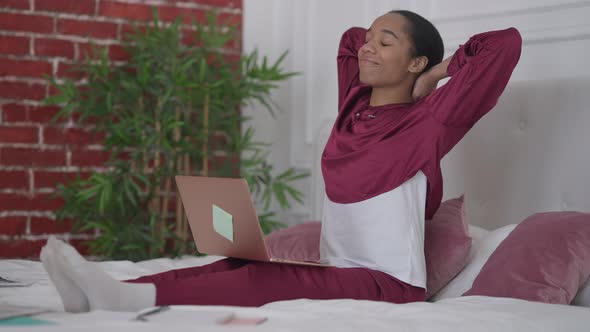 Wide Shot of Young Happy African American Woman in Pajamas Stretching Sitting on Bed Checking Email