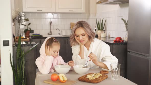 Mother and Little Daughter Sitting at the Kitchen Table Do Not Want To Eat Oatmeal Porridge with