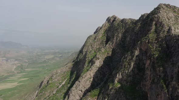 Aerial Drone Footage of Majestic Rock with Green Vegetation Against Misty Valley at Background