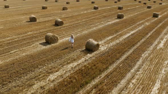 Beautiful young girl in a white shirt on a field among sheaves of hay. Aerial view	