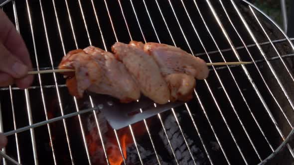 Hand Is Placing Wooden Skewer with Delicious Chicken Wings on the Grill Grid