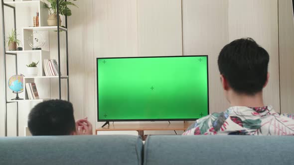 Father And His Son Are Watching Green Mock-Up Screen Tv While Sitting On A Couch At Home