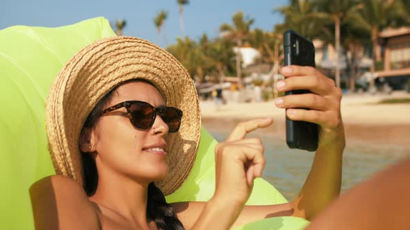 Young Woman Using Mobile Phone App and Relaxing on Inflatable Mattress in Sea. Slowmotion Travel