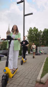 Fashionable charming group of friends riding public rental electric scooters