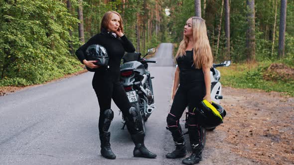 Women Friends Standing Near the Motorbikes in the Forest Holding Helmets and Talking