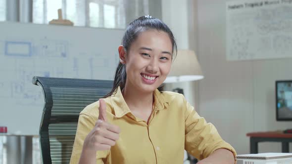 Asian Woman Engineer With Blueprint Warmly Smiling And Showing Thumb Up To Camera At The Office