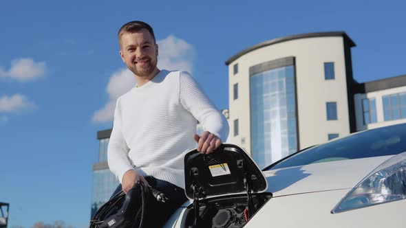 A Fairskinned Male Driver Holds a Charging Cable for an Electric Car