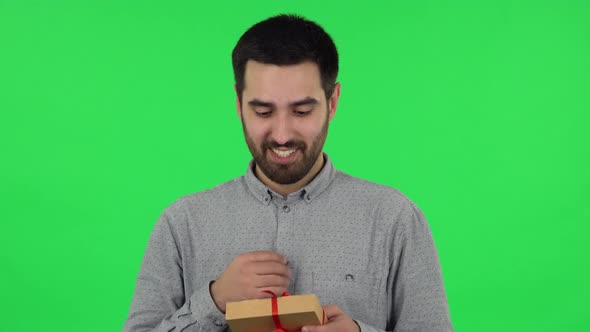 Portrait of Brunette Guy Is Opening the Gift, Surprised and Rejoicing. Green Screen