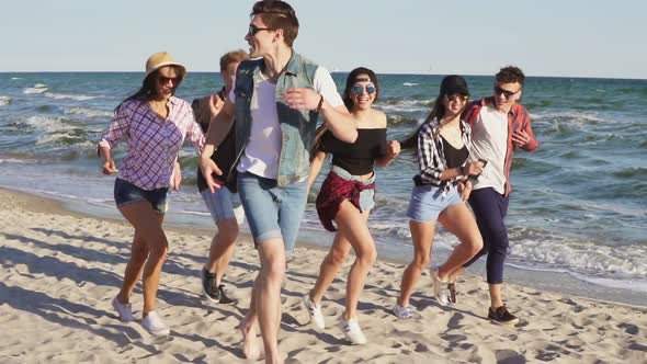 Group of Young Hipster Friends Running Together on a Beach at the Water's Edge