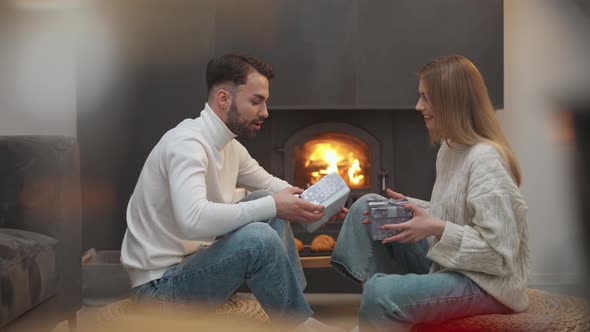 Romantic Holiday Cheerful Guy and a Female Exchange Boxes with Gifts a Young Couple is Sitting By