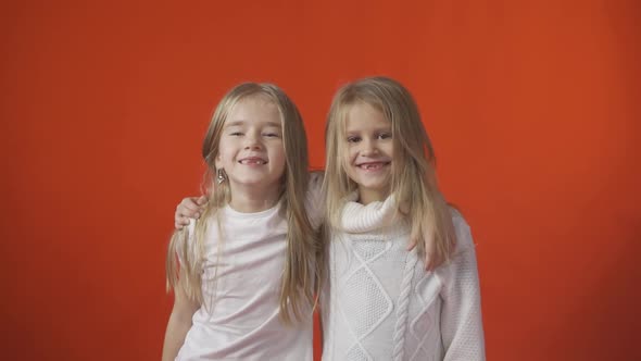 Two Little Toothless Girls are Smiling Against an Orange Background