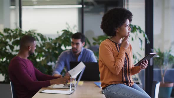 Diverse business people sitting using laptops going through paperwork in office