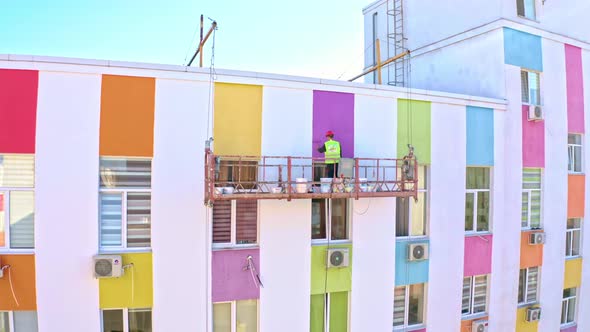 A Worker Paints The Facade Of A Building At A Height
