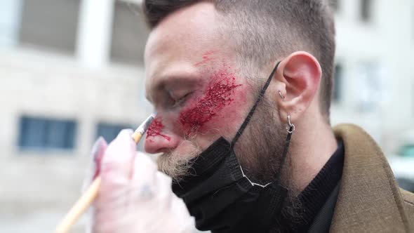 Anonymous makeup artist putting makeup on the face of a hipster man