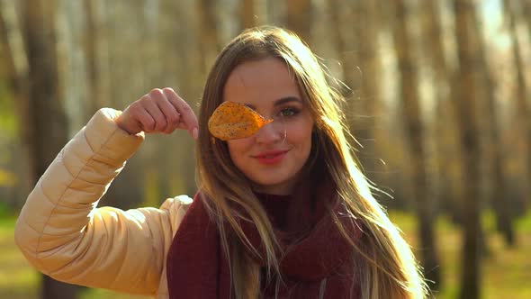 Young Attractive Girl in Autumn Park, Playing with a Leaf on her Face.