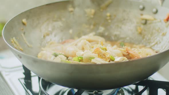 Woman stirring hot wok noodles with chopsticks